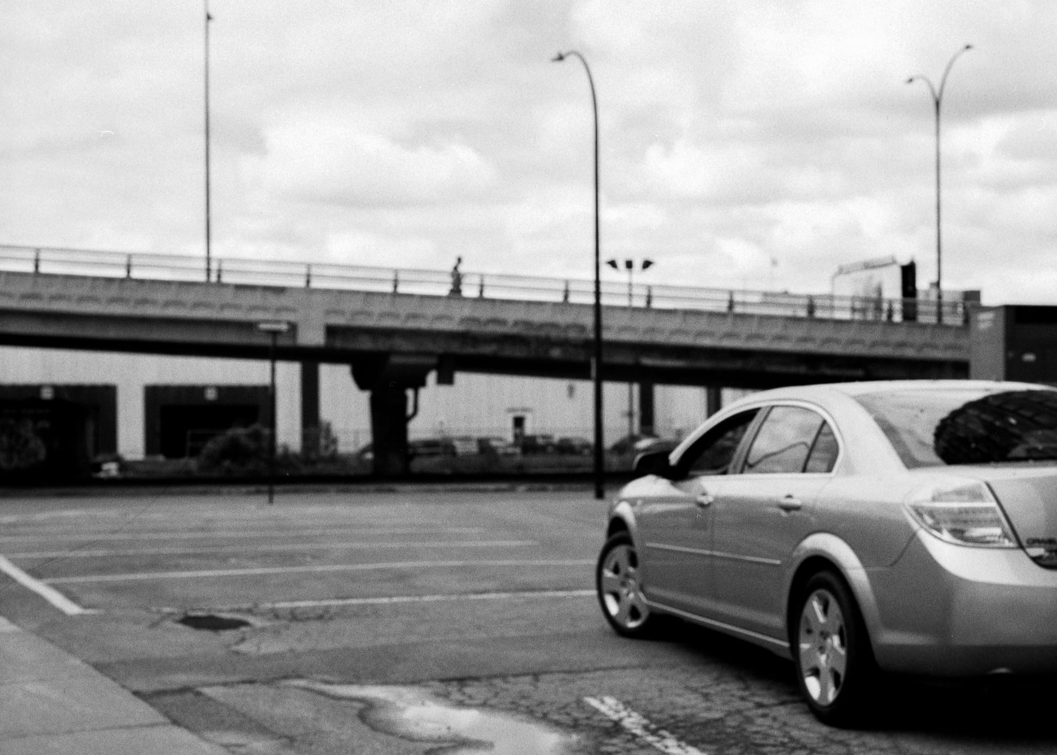 A car parked to the right of the frame with an overpass in the background